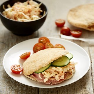 A plate with sliced pitta bread containing ham, coleslaw and cucumbers. Served with cherry tomatoes cut in half.