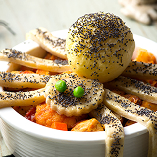 Pastry spider with peas as eyes, sat on-top of a chicken pie
